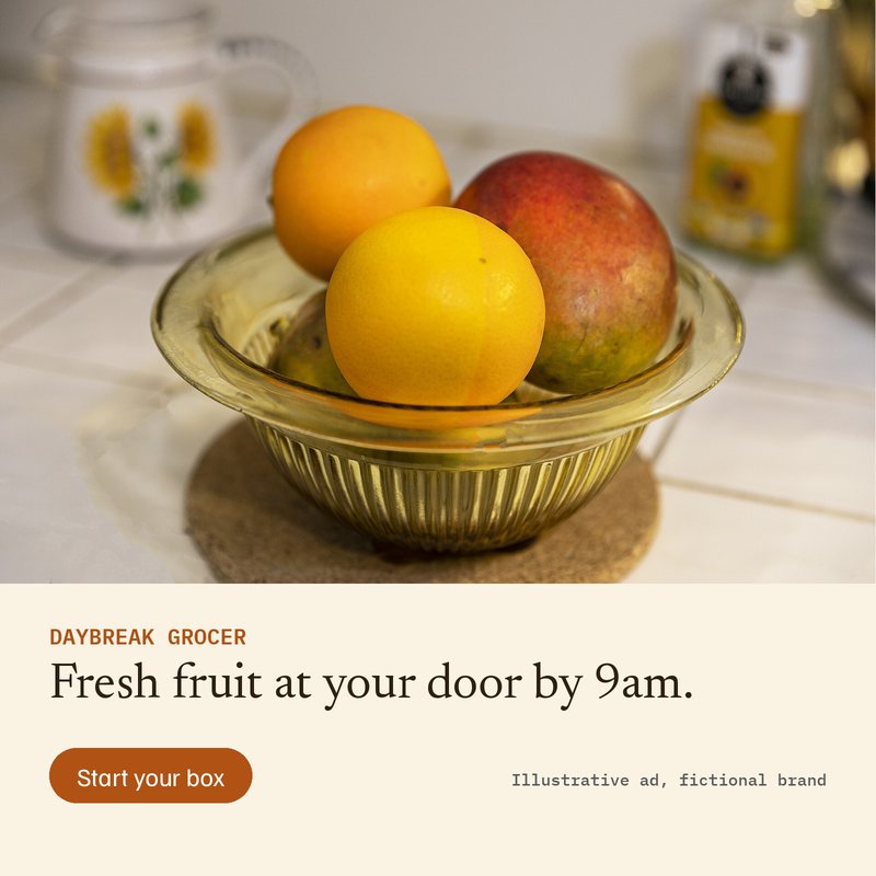 Ad A for Daybreak Grocer (fictional): photo of a glass bowl with oranges and a mango on a white tiled kitchen counter, headline Fresh fruit at your door by 9am, button Start your box.